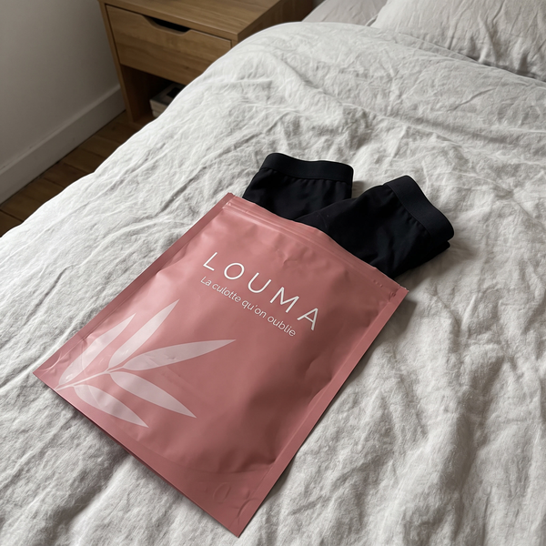Pochette Louma ouverte sur un lit, deux culottes noires à côté