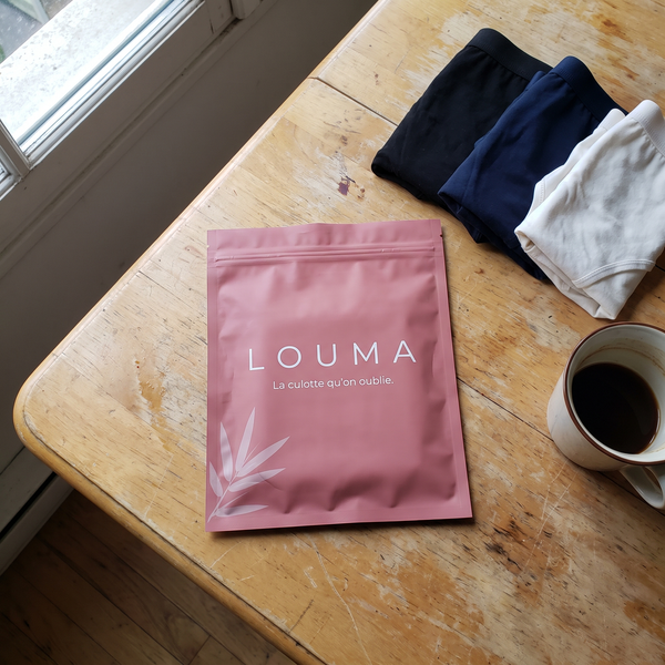 Pochette Louma sur une table de cuisine, trois culottes pliées et une tasse de café