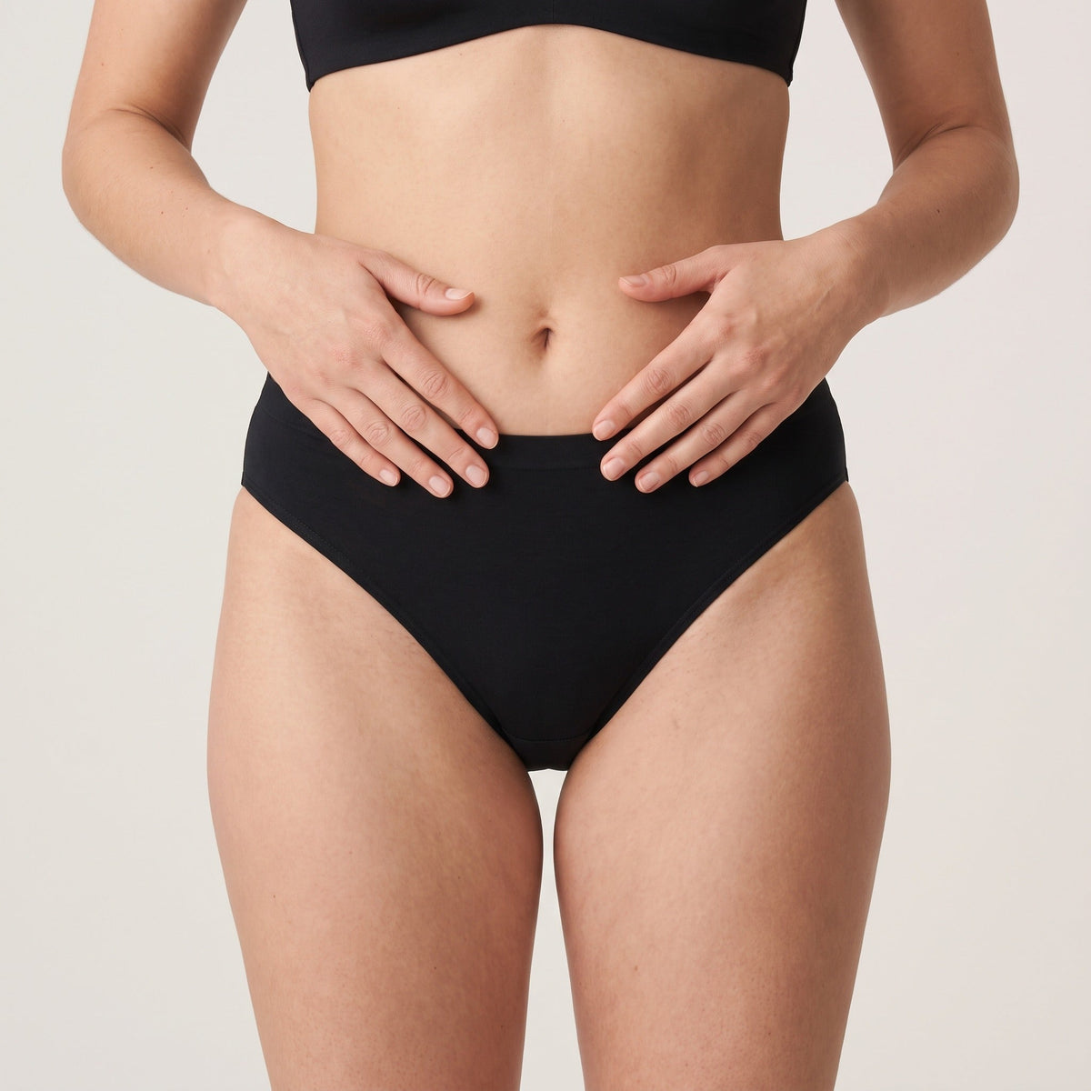 Culotte échancrée Louma noire portée, vue de face, mains posées sur le ventre